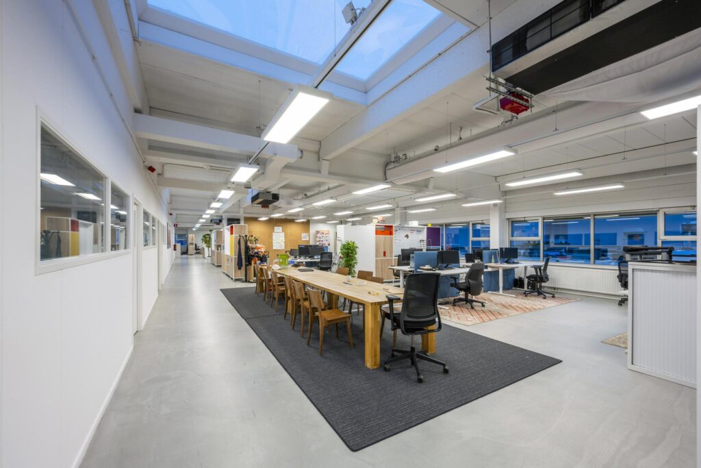 Modern open kantoorinterieur aan de Van der Madeweg met werkplekken, vergadertafel en grote ramen.